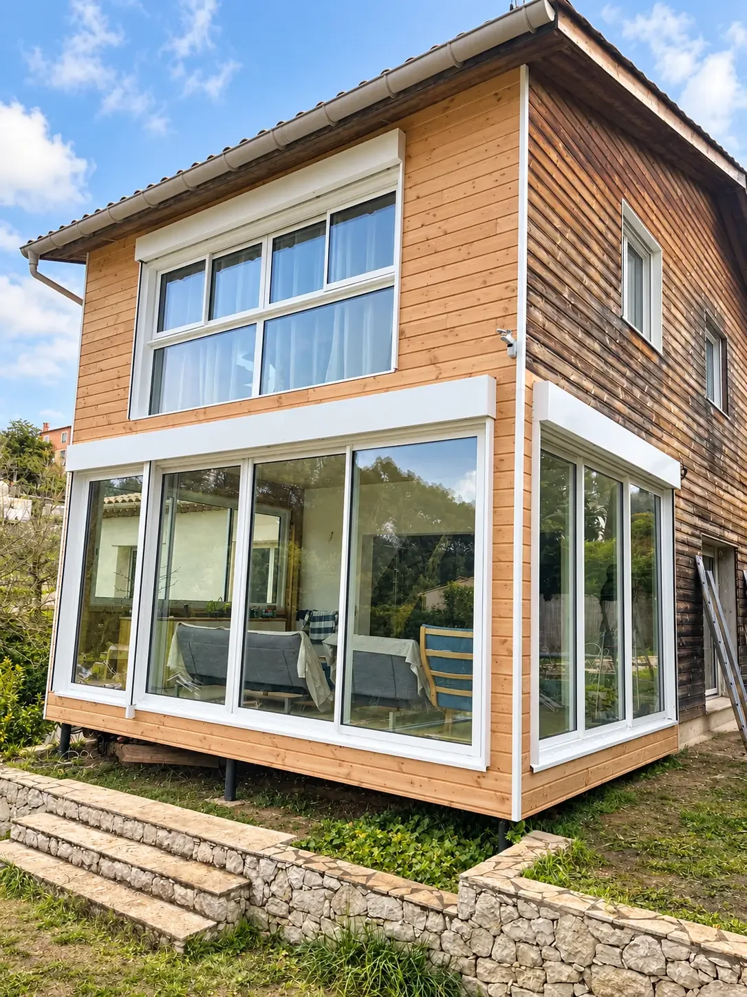 Façade vitrée au rez-de-chaussée d’une maison à bardage bois.