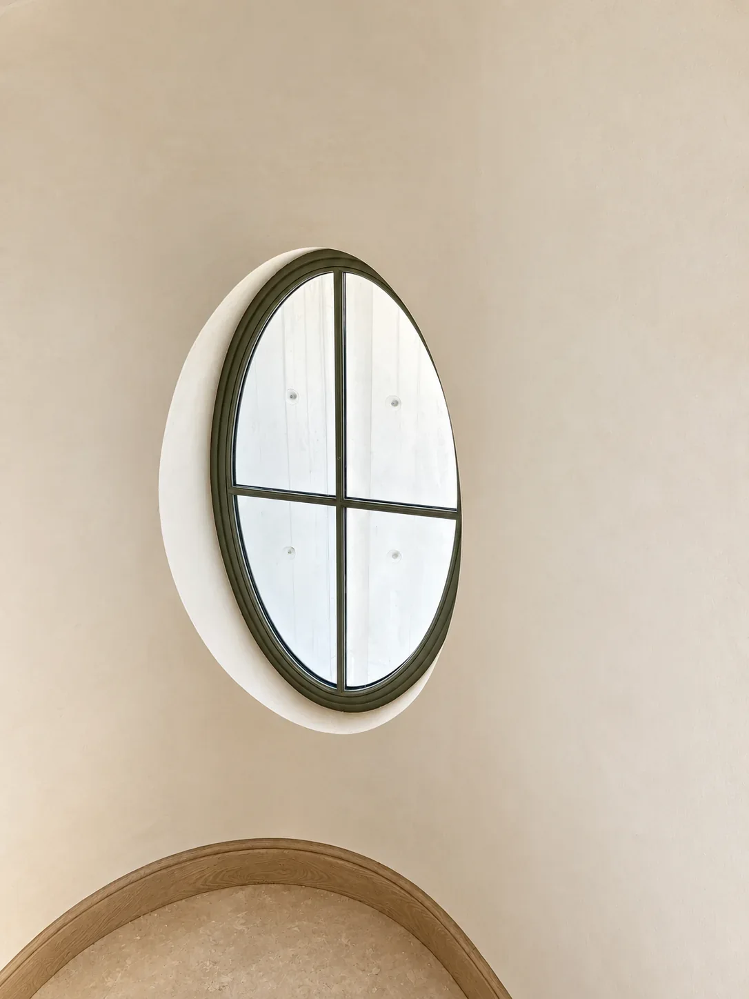 Fenêtre ovale à croisillons dans un mur intérieur clair.