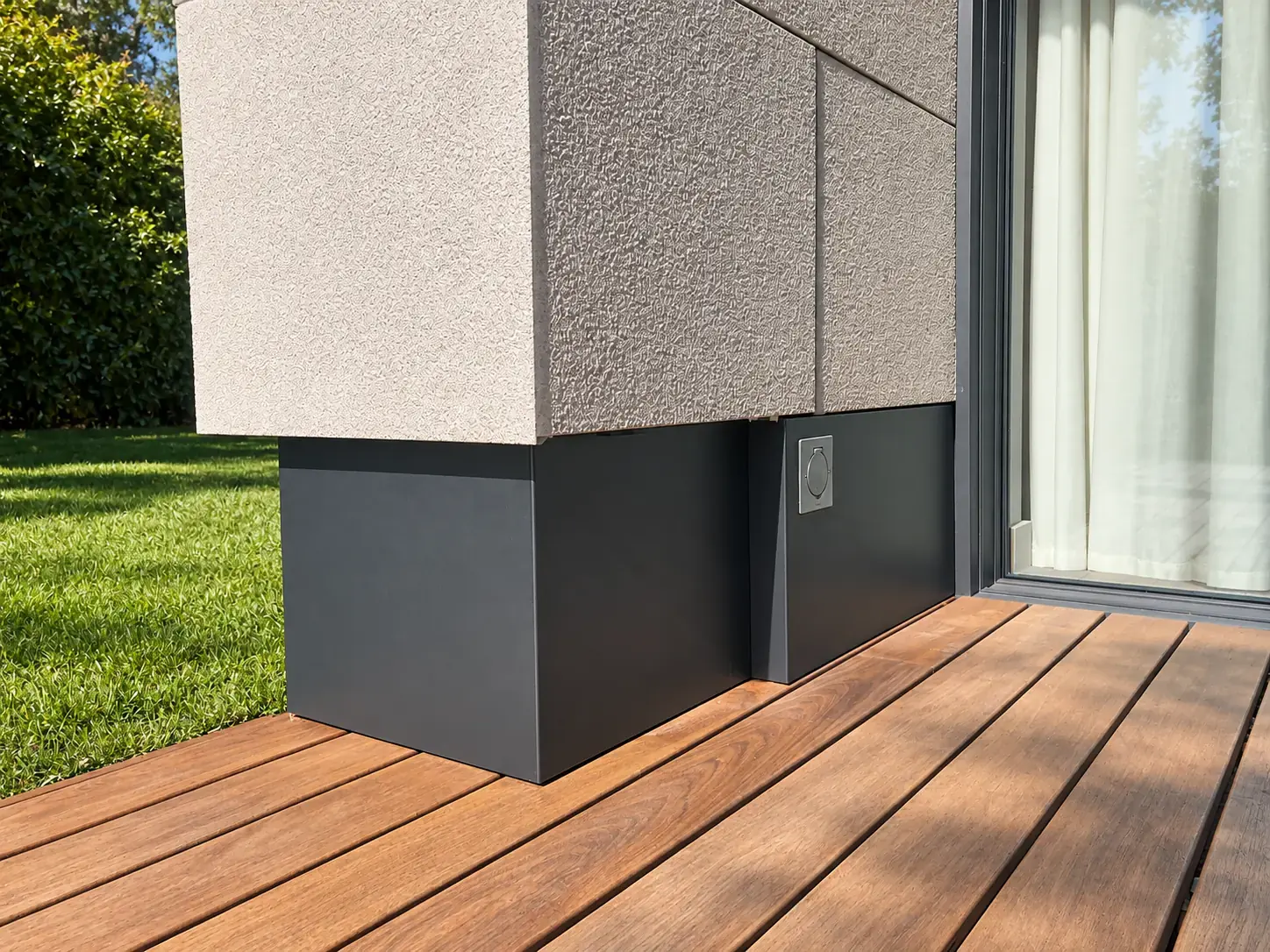 Habillage anthracite en pied de façade, près d’une baie vitrée et d’une terrasse en bois.