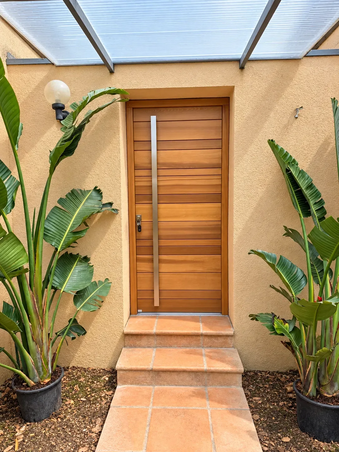 Porte d’entrée aspect bois avec longue poignée verticale, protégée par un auvent.