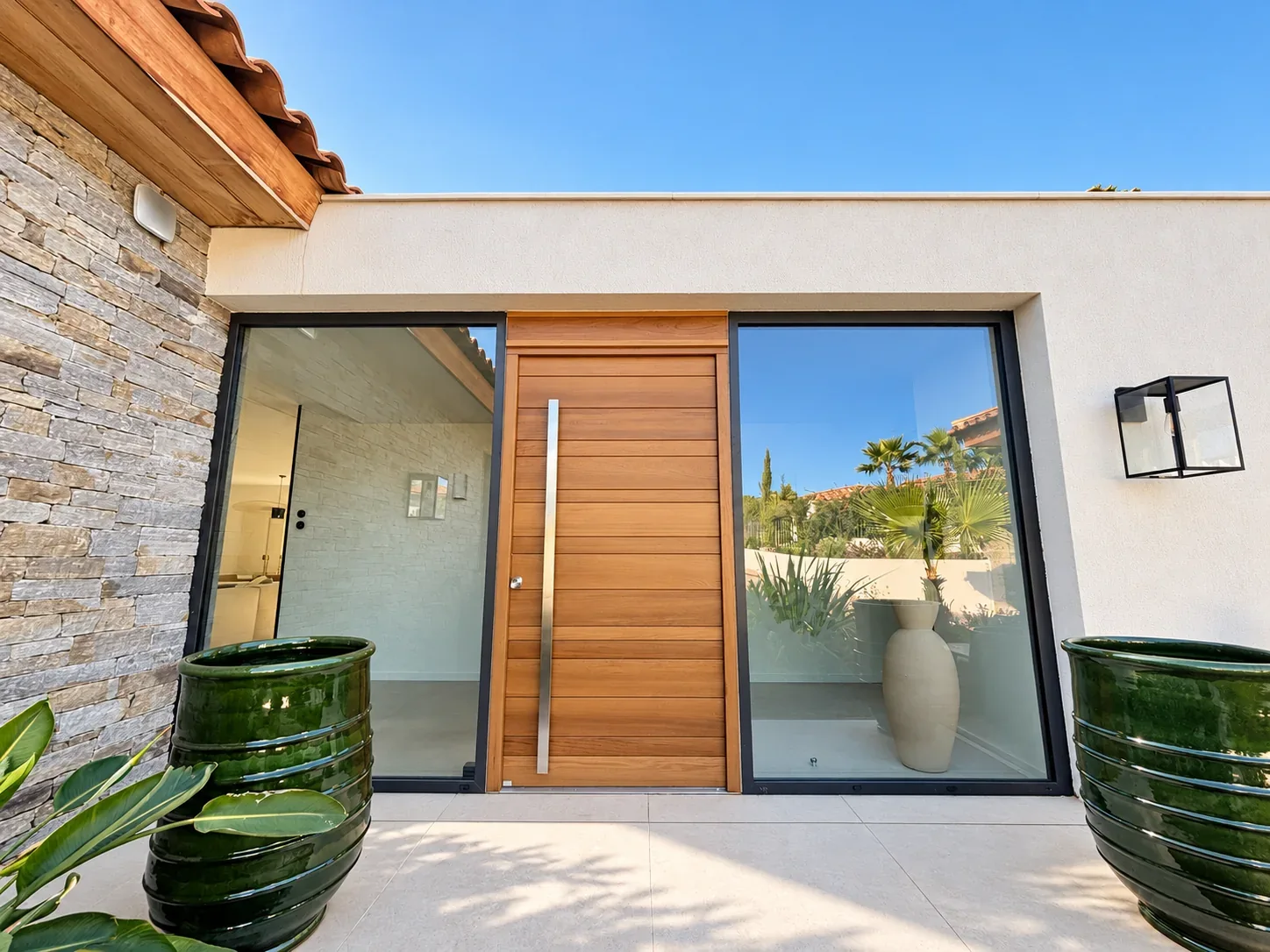 Porte d’entrée en bois avec vitrages latéraux et grands pots verts.