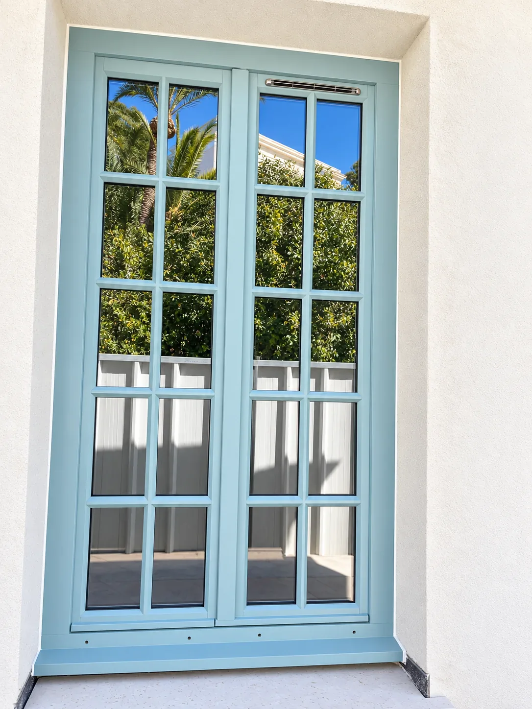 Porte-fenêtre bleue à petits bois sur une façade claire.