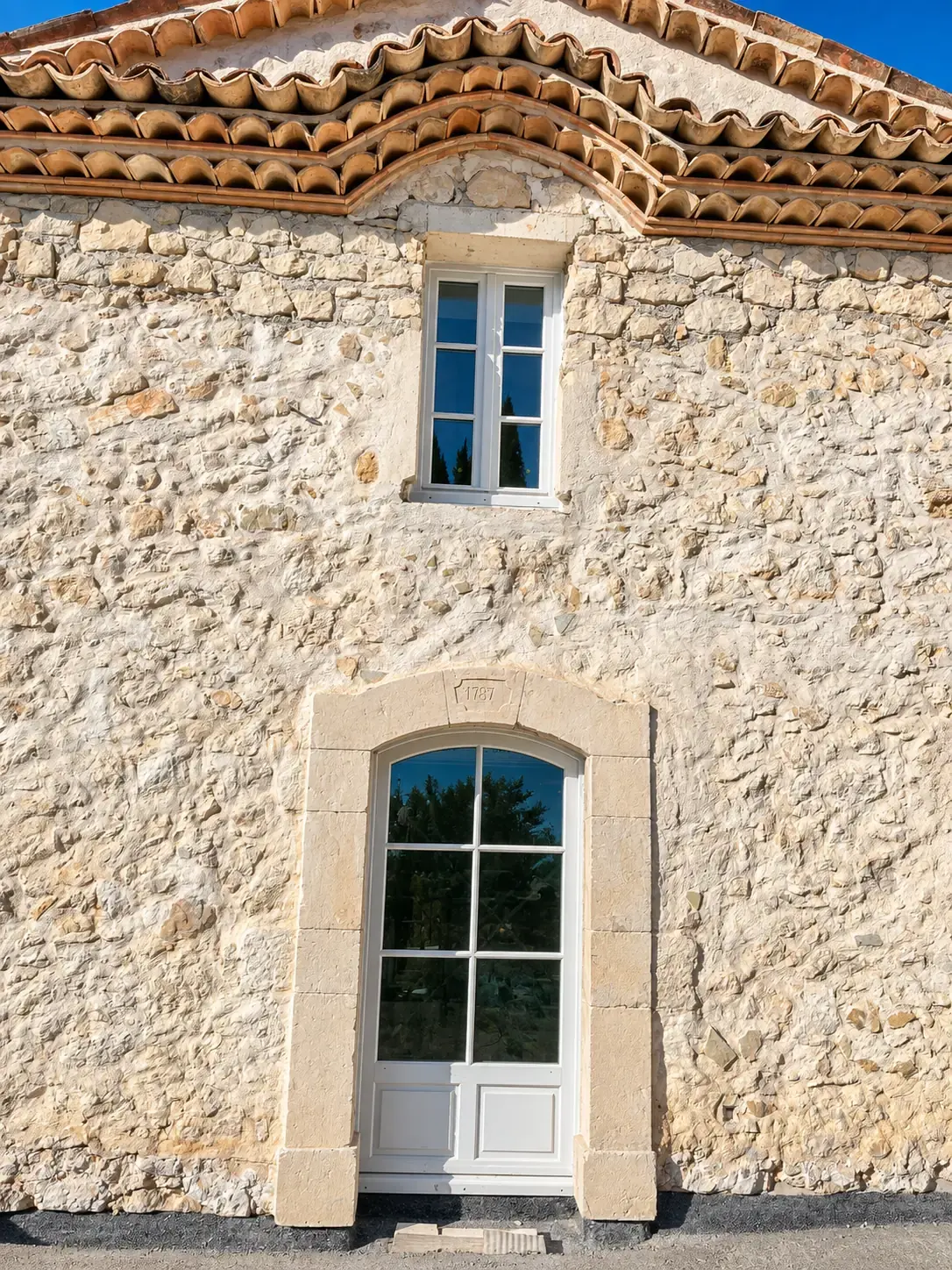 Porte vitrée et fenêtre sur la façade d’une maison en pierre.