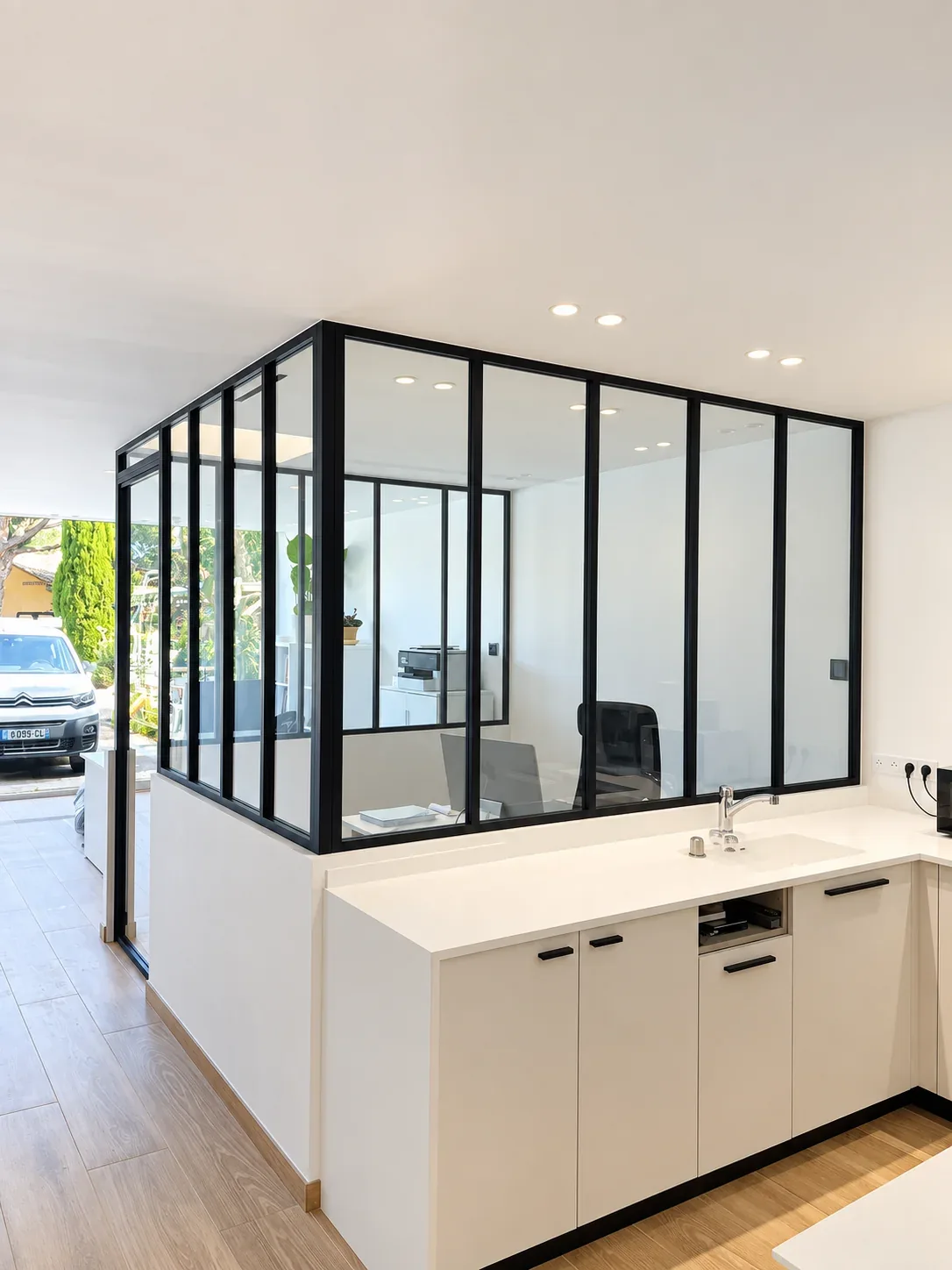 Verrière à montants noirs séparant un bureau d’un espace de circulation.